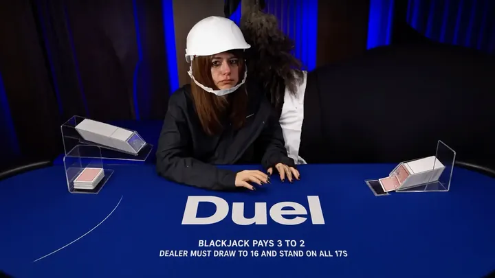 Annika dealing Duel Blackjack in a white hard hat, hands on the blue felt