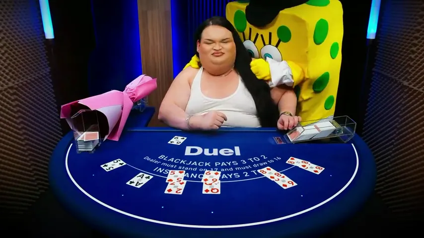 The yellow costume standing beside a seated guest with a wrapped pink bouquet at the Duel Blackjack table