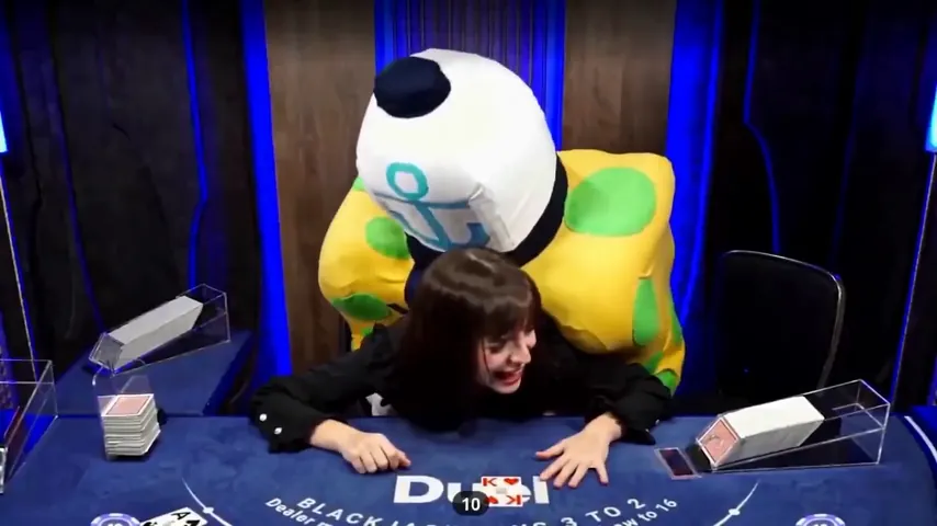 The costume leaning over a seated guest at the Duel Blackjack table from behind